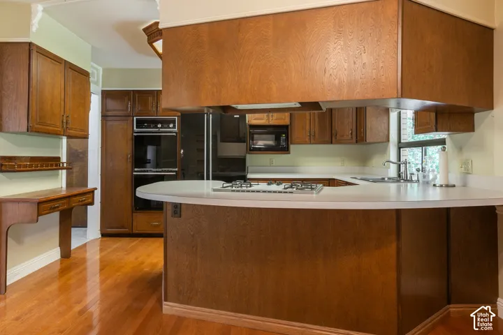 Chef's kitchen featuring rich wood cabinetry, stainless steel appliances including a gas cooktop and built-in wall oven, white quartz countertops, and a curved island with seating
