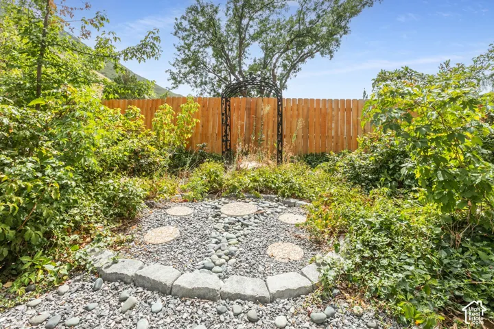 Landscaped garden area featuring a wood fence, decorative metal archway, and a gravel and stone paver path