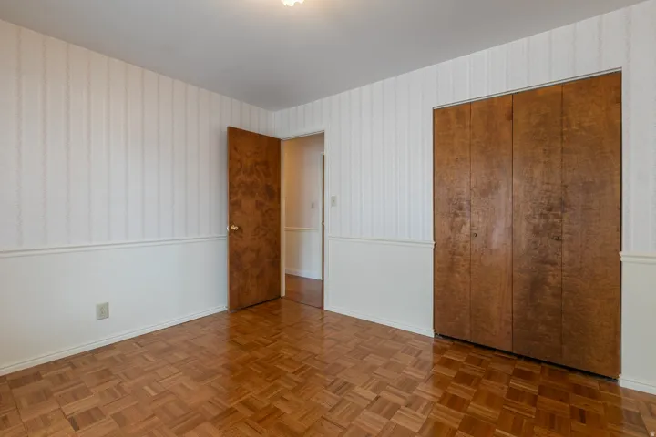 Parquet wood flooring, a built-in closet with wood doors, and a wood-paneled door with a brass-finish knob
