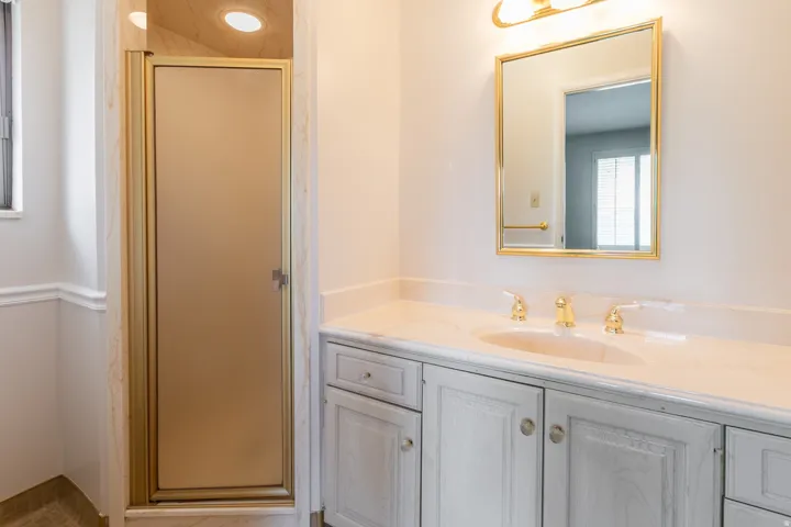 Vanity with integrated sink and gold-tone fixtures, wall-mounted mirror with gold-tone frame, painted cabinetry, and a shower enclosure with a frosted glass door and gold-tone frame