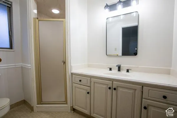 Bathroom vanity featuring a light-toned wood-finish cabinet, stone-look countertop, integrated sink, and matte black faucet, accompanied by a framed mirror, vanity lighting, and a shower enclosure with a frosted glass door