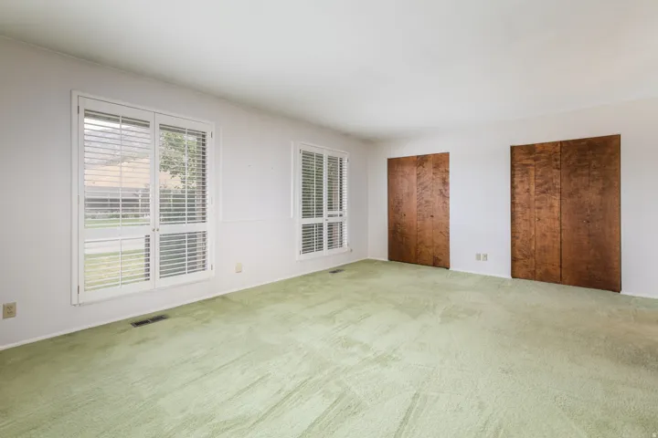 Spacious room featuring dual windows with white plantation shutters and two sets of wood-paneled bi-fold closet doors
