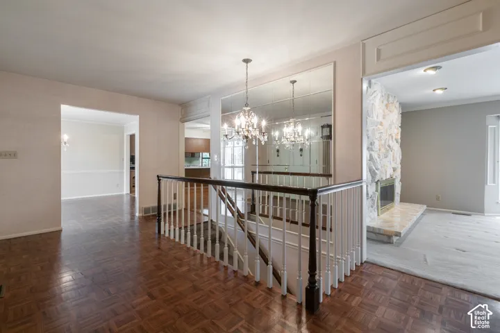 Hardwood parquet flooring, built-in mirror wall, chandelier lighting, staircase with dark wood railing, and a stone-faced fireplace