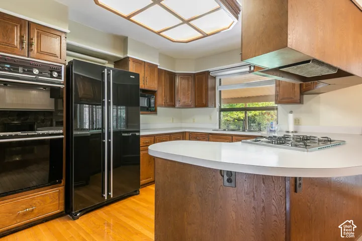 Wood-finish cabinetry, built-in oven, black side-by-side refrigerator, white countertops, and wood-finish flooring