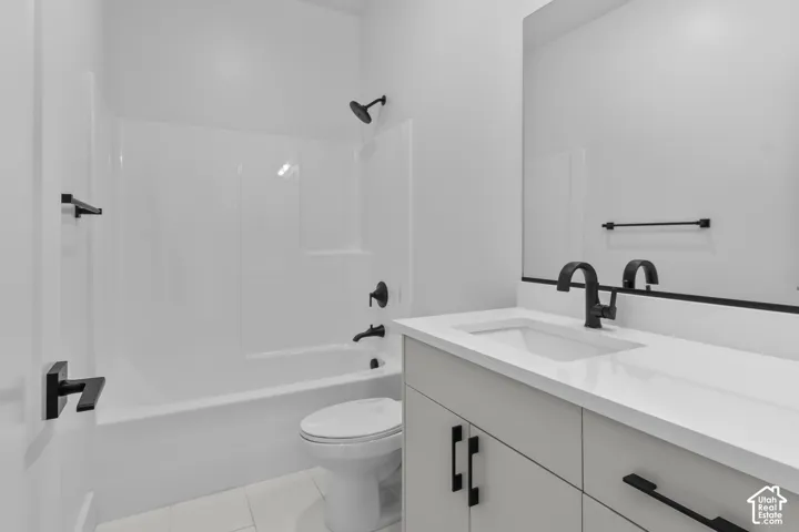 White tile flooring, white bathtub and shower surround, black matte fixtures, white countertop, and gray vanity cabinetry