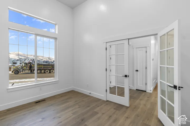 Wood-finish flooring, white walls, and French doors with matte black hardware