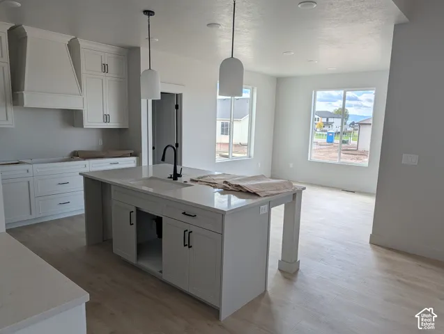 Kitchen featuring white shaker-style cabinetry, quartz countertops, a central island with a matte black faucet, and wood-finish flooring
