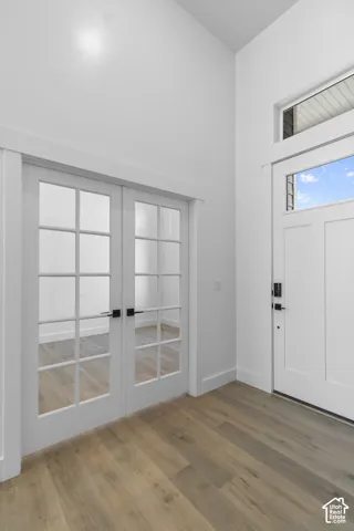 White interior walls, wood-finish flooring, white paneled entry door, transom window, and double french doors with matte black hardware