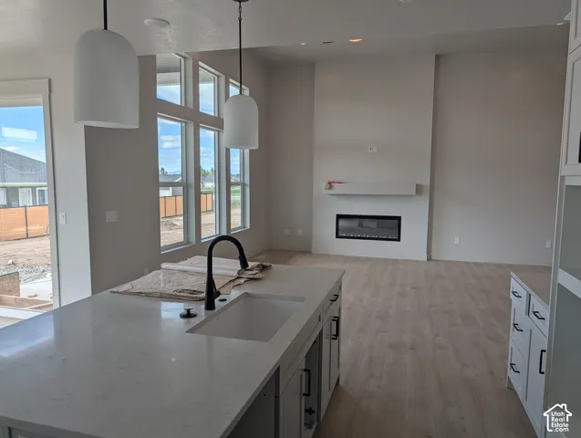 Kitchen island featuring stone-surface countertops, undermount sink, and matte black faucet, complemented by dual pendant lighting, wood-finish flooring, and a floor-to-ceiling fireplace mantel