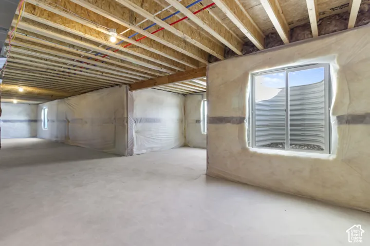 Unfinished lower level with exposed ceiling joists, concrete flooring, and multiple window wells providing natural light