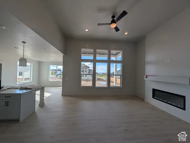 Open-concept interior featuring tall ceilings, wood-finish flooring, a linear electric fireplace with a floating mantel, and oversized windows
