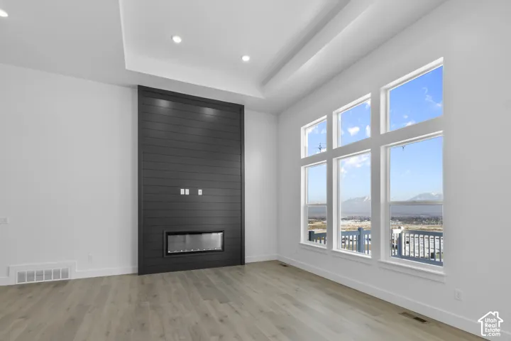Vaulted ceiling, recessed lighting, expansive windows, built-in electric fireplace, and wood-finish flooring