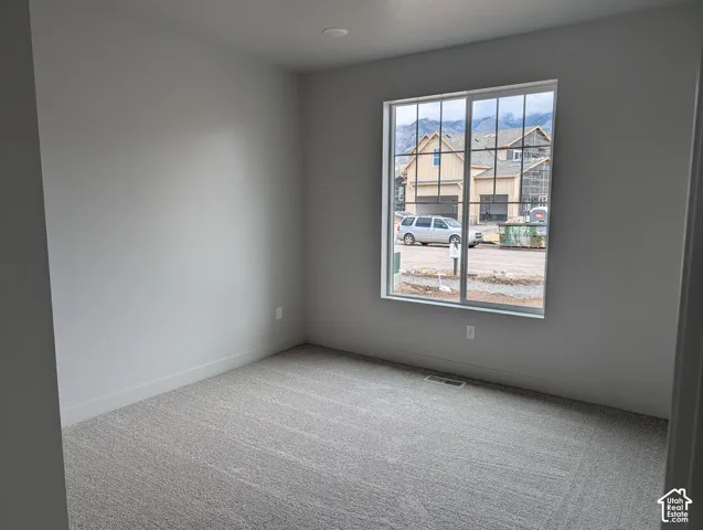 Neutral-toned interior space featuring light-colored wall paint, carpeted flooring, and a large grid-patterned window with exterior mountain scenery