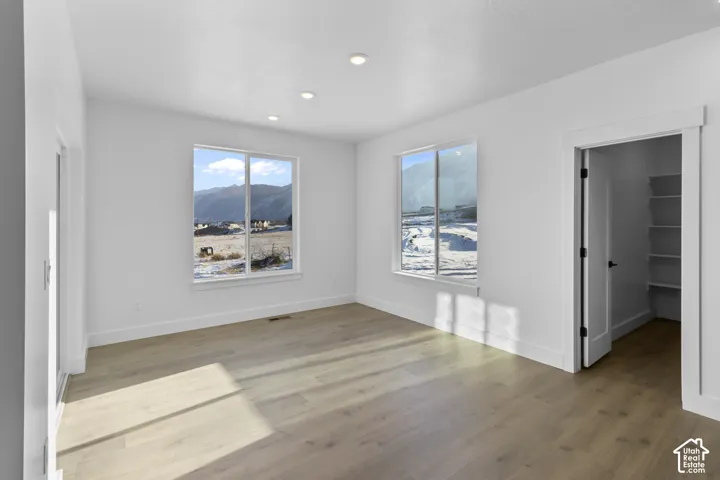 Recessed lighting, wood-finish flooring, two large windows, white trim, and a closet with built-in shelving