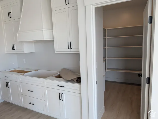 White shaker-style cabinetry with matte black hardware, custom range hood, and walk-in pantry with integrated shelving