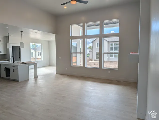 High-ceiling living area featuring large windows, wood-finish flooring, a ceiling fan, and a kitchen island with pendant lighting