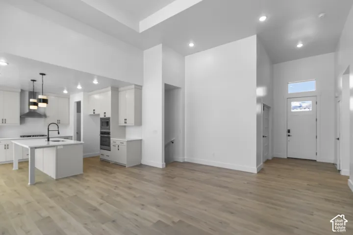 Expansive open-concept living area with wood-finish flooring, recessed lighting, and a white front door with transom window