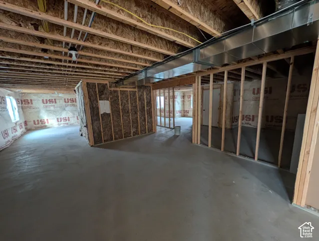 Unfinished interior space featuring exposed wood-framed walls, concrete flooring, insulated wall segments, and overhead metal ductwork