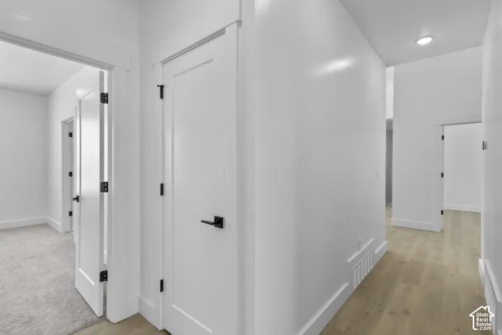 White interior doors with black hardware, light wood-finish flooring, recessed lighting, and crisp white baseboards
