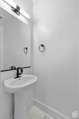 Pedestal sink with a matte black faucet, wall-mounted mirror, and an overhead vanity light fixture