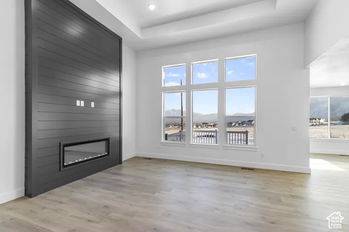 Wood-finish flooring throughout, modern horizontal fireplace, expansive windows, tray ceiling, and recessed lighting