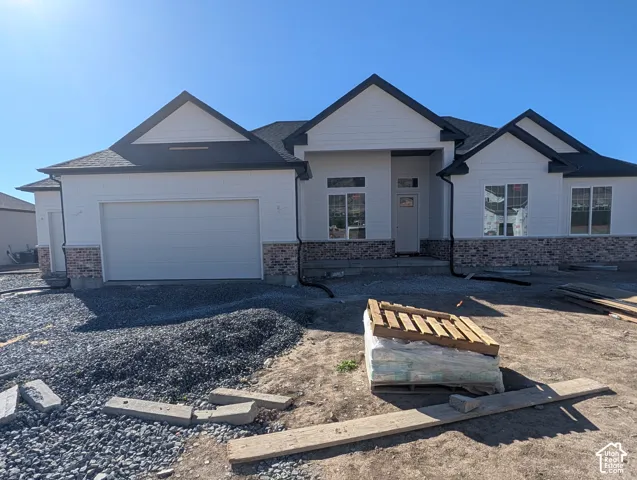 Exterior featuring white siding, dark shingle roof, integrated garage, and brick detailing