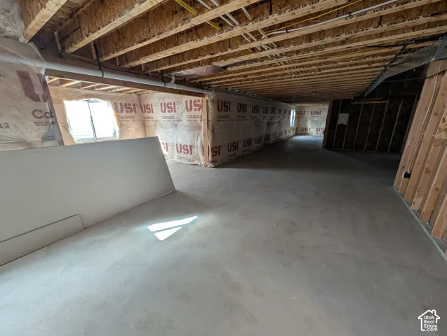 Unfinished interior space featuring concrete slab flooring, exposed wood joist ceilings, insulated walls, and two slider windows