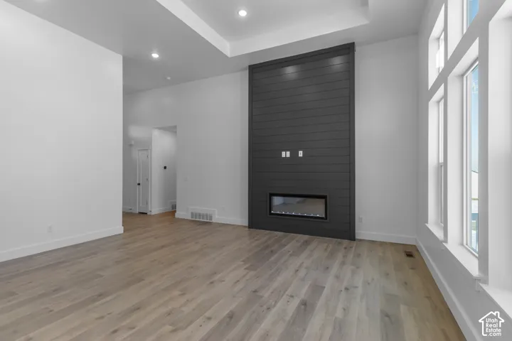 Contemporary living area featuring wood-finish flooring, a linear electric fireplace, and a tray ceiling with recessed lighting