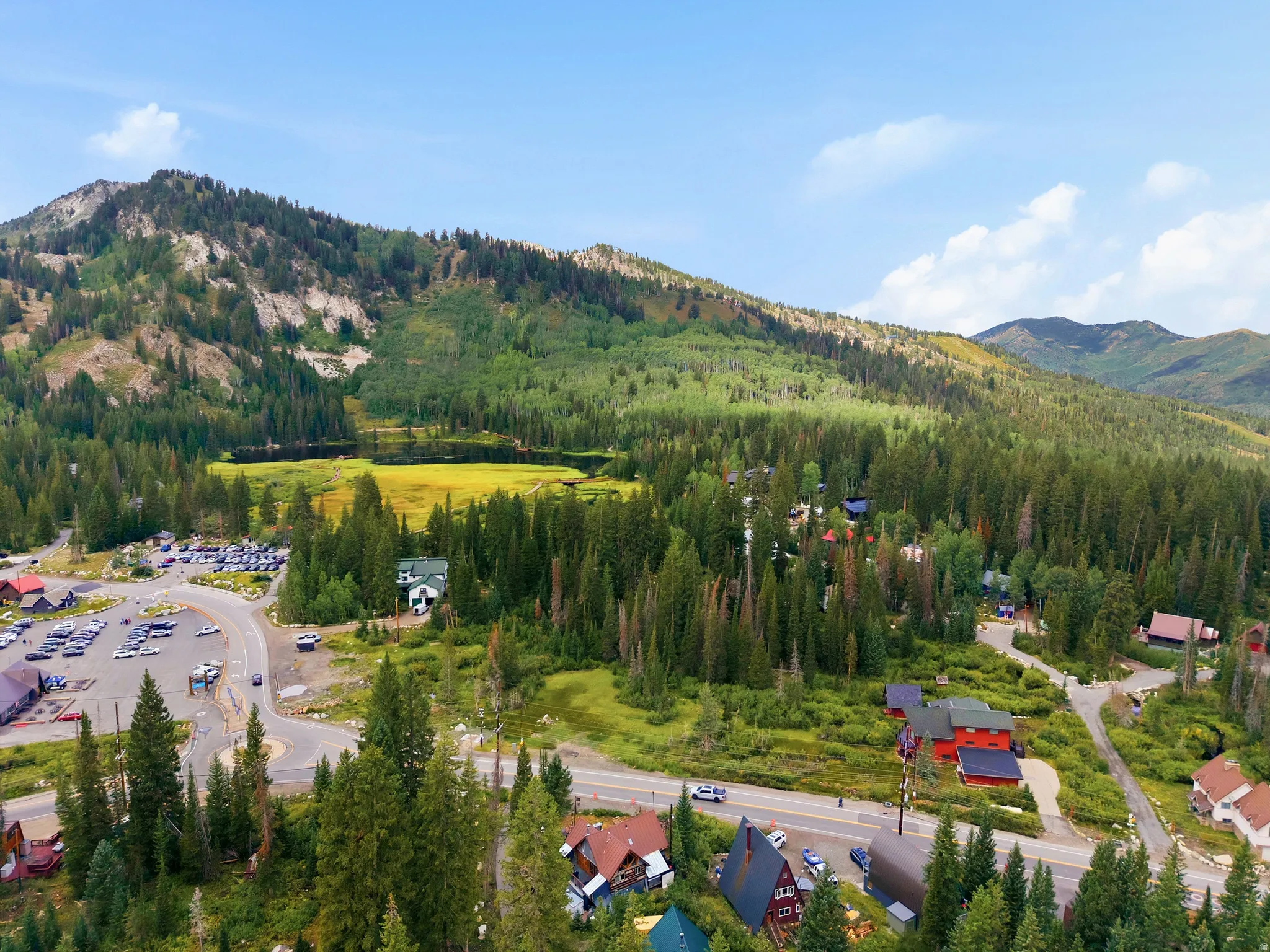 Mountainous terrain with extensive tree coverage, featuring a visible body of water, residential structures, and paved roadways