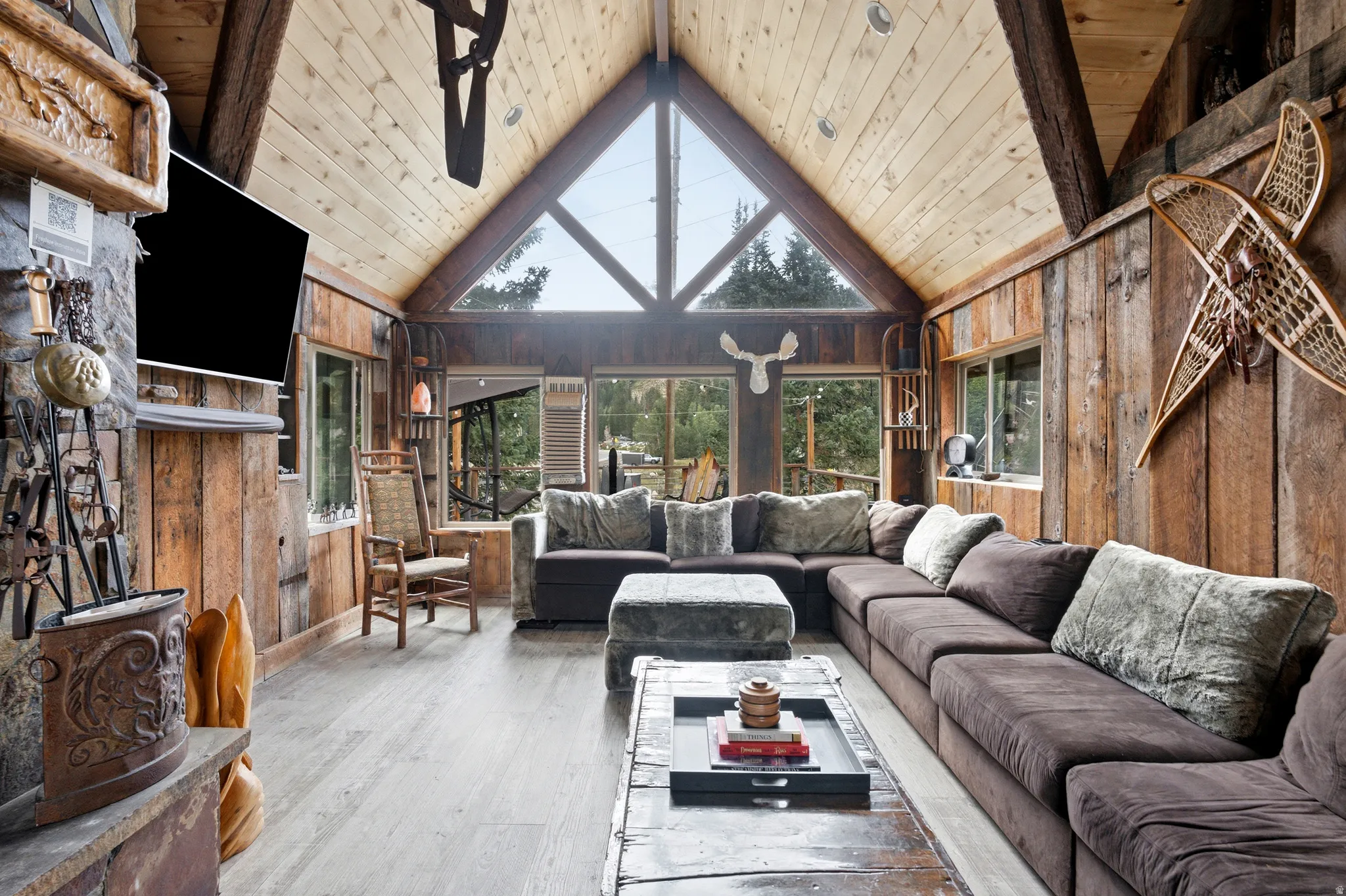 Vaulted wood-paneled ceilings, exposed wood beams, stone fireplace, large triangular window, and wood-finish flooring