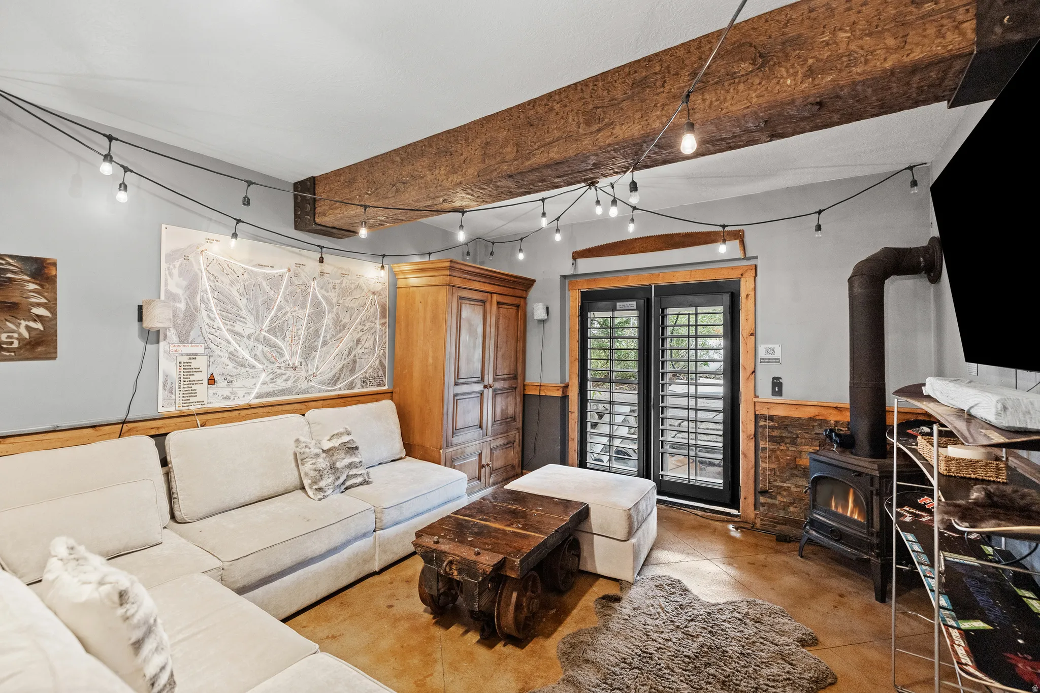 Exposed wood beams, wood-burning stove, concrete flooring, wood paneling, and a wood cabinet