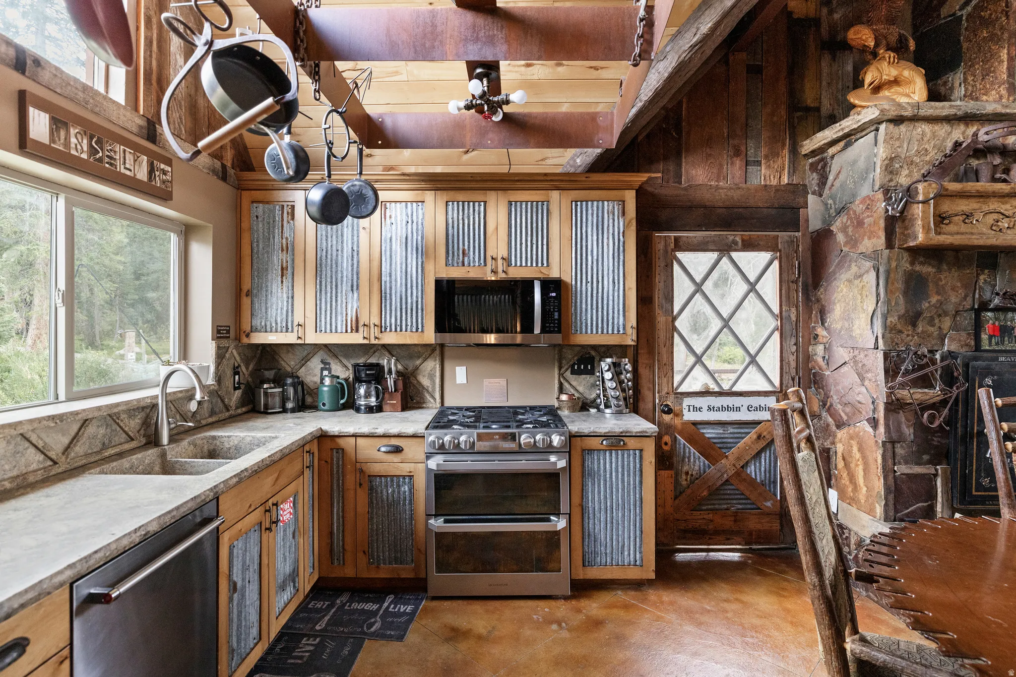 Kitchen featuring wood cabinetry with corrugated metal inserts, stainless steel appliances, stone-finish countertops, and a double basin sink