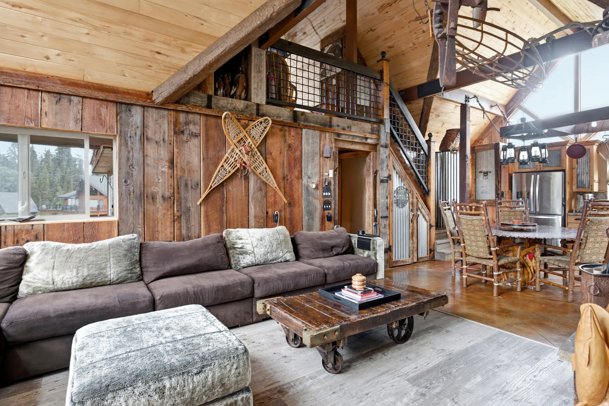 Vaulted wood-paneled ceiling, exposed wood beams, wood-plank accent wall, industrial-style staircase with metal railing, and a dining area with a chandelier