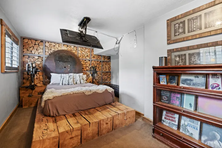 Custom wood block bed frame, unique wood-panel accent wall, integrated wall-mounted television, and wood-framed window with shutters