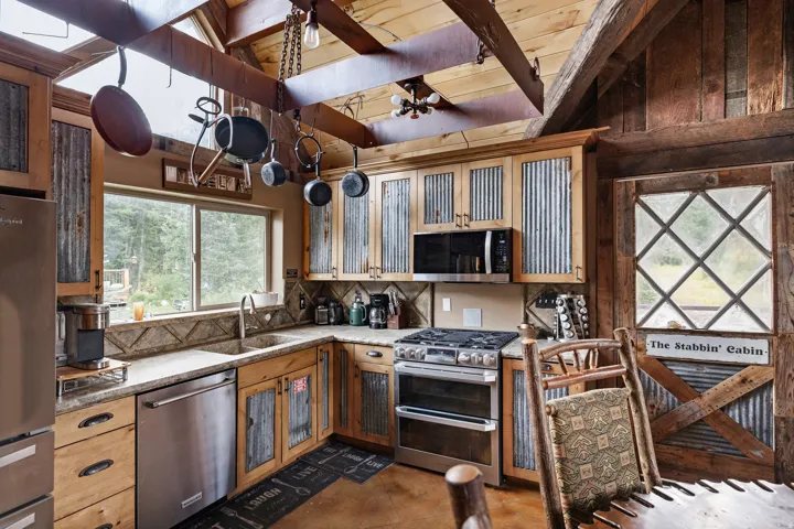 Kitchen featuring wood cabinetry with corrugated metal panel inserts, stainless steel appliances, granite countertops, and a wood-beamed ceiling