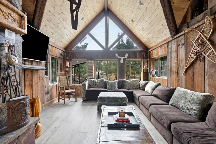 Vaulted wood-paneled ceilings, exposed wood beams, stone fireplace, large triangular window, and wood-finish flooring