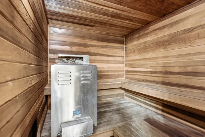 Wood-paneled sauna featuring a stainless steel heater, integrated stone elements, and built-in wood benches