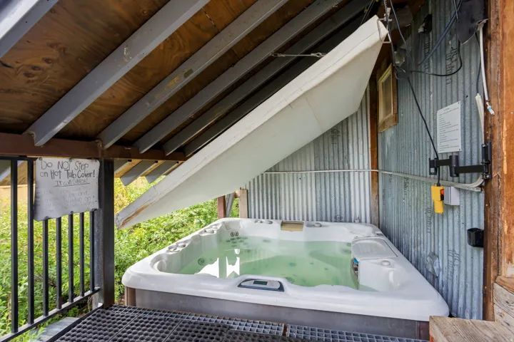 Outdoor spa with a lifting cover mechanism, corrugated metal siding, and wood ceiling with exposed beams