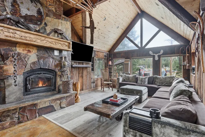 Vaulted wood-paneled ceiling, stone-clad fireplace with carved wood mantel, wood-finish flooring, and expansive triangular windows