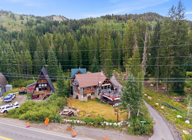 Wooded hillside property featuring two distinct structures, a large wood deck, and a paved driveway