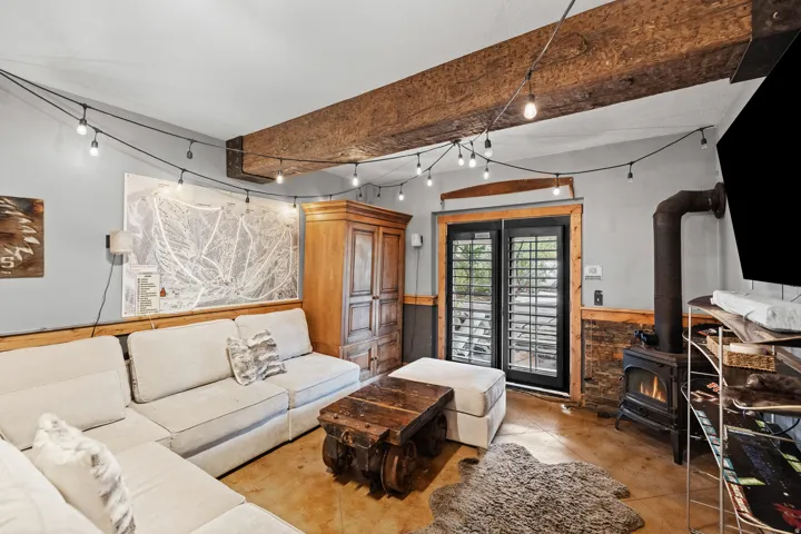 Exposed wood beams, wood-burning stove, concrete flooring, wood paneling, and a wood cabinet