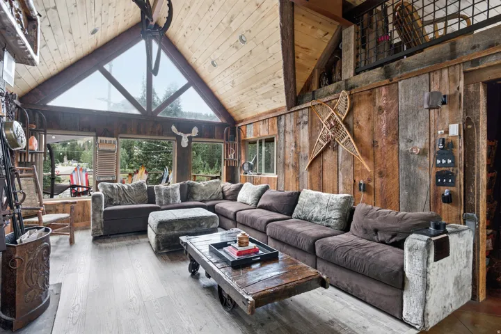 Vaulted wood-paneled ceilings, large A-frame windows, wood-finish flooring, wood-paneled walls, and an upper-level interior balcony with metal railing