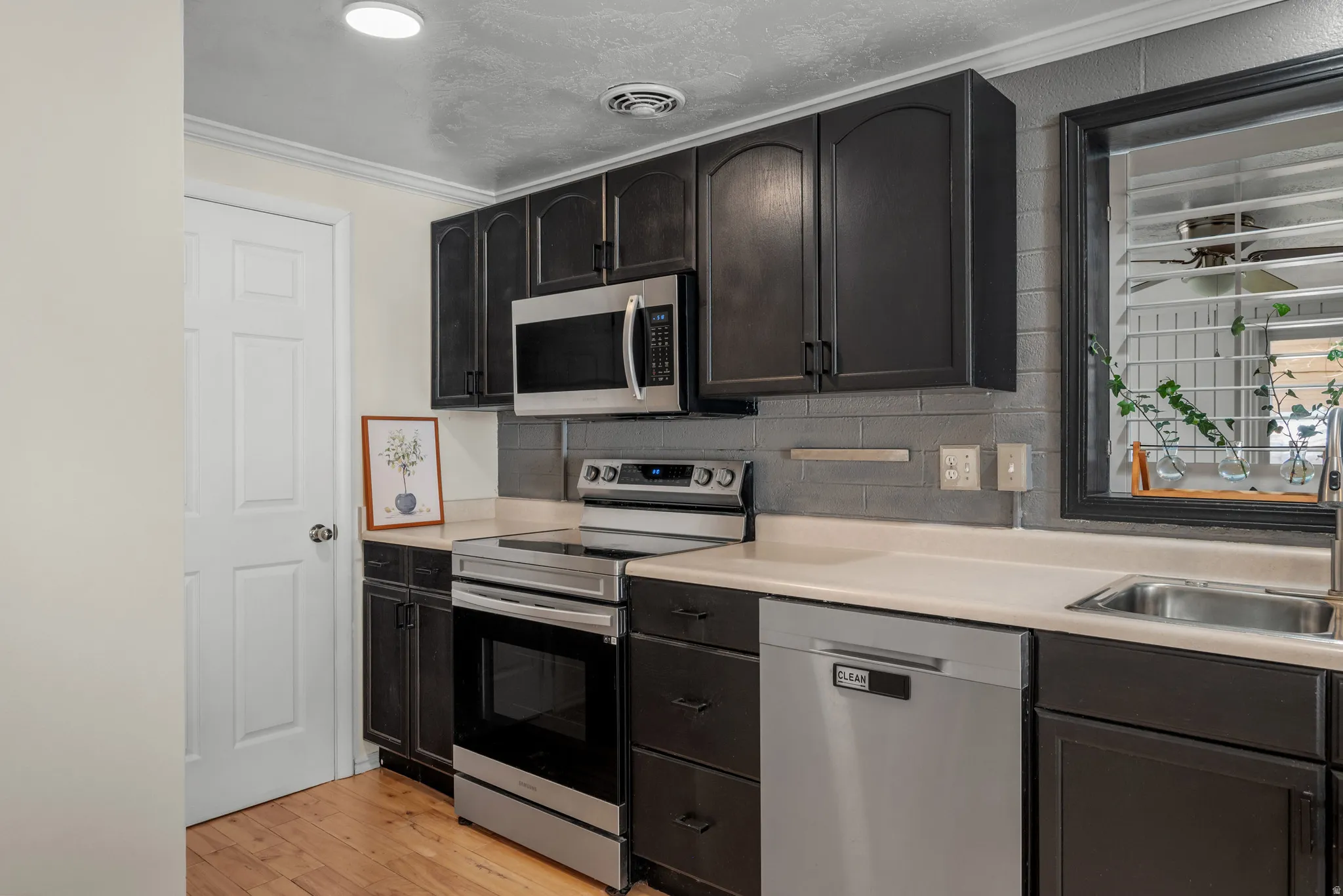 Dark cabinetry, stainless steel appliances, light countertops, subway tile backsplash, and wood-finish flooring