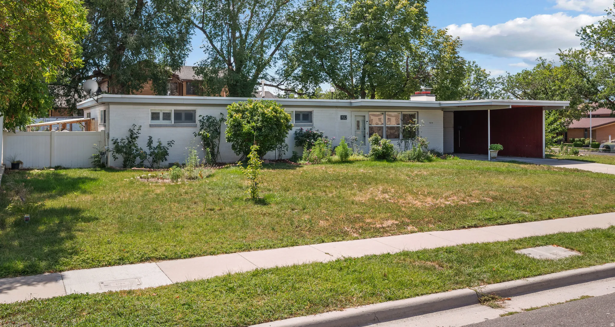 Single-story residence featuring a carport, a front sidewalk, and a partially fenced perimeter