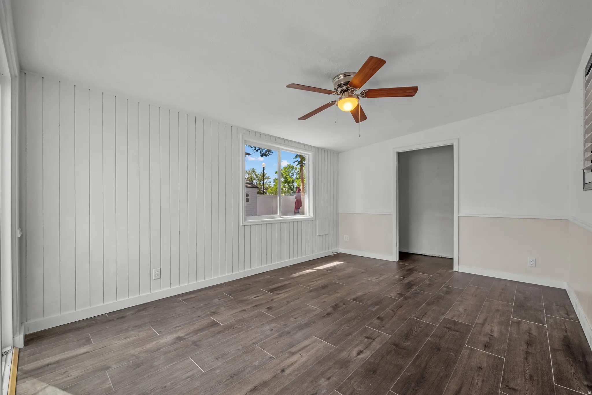 Wood-finish tile flooring throughout, white vertical plank wall paneling, and a ceiling fan with light fixture