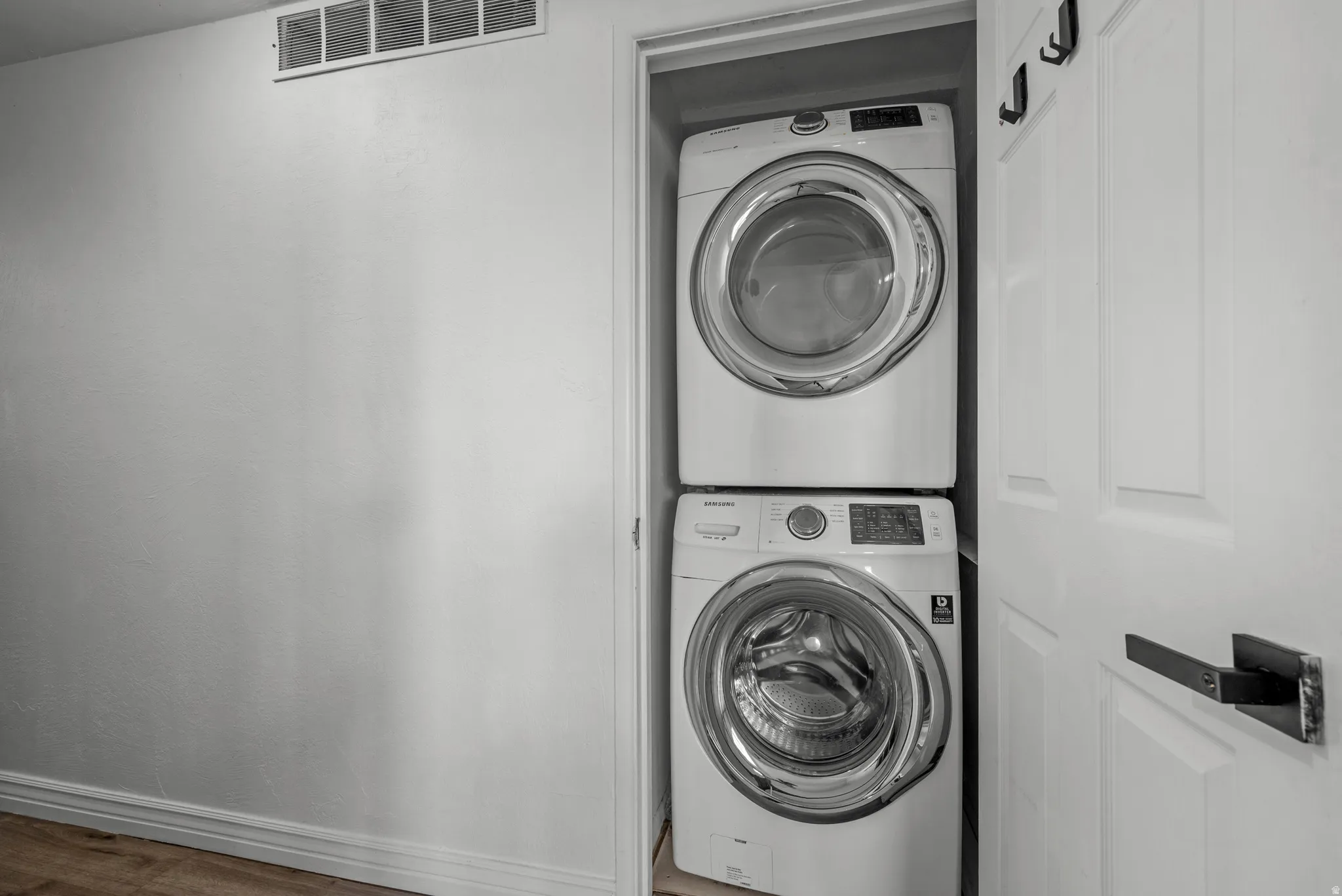 Stackable front-load washer and dryer set in a dedicated utility closet, featuring a white paneled door with a contemporary black lever handle and wall-mounted hooks