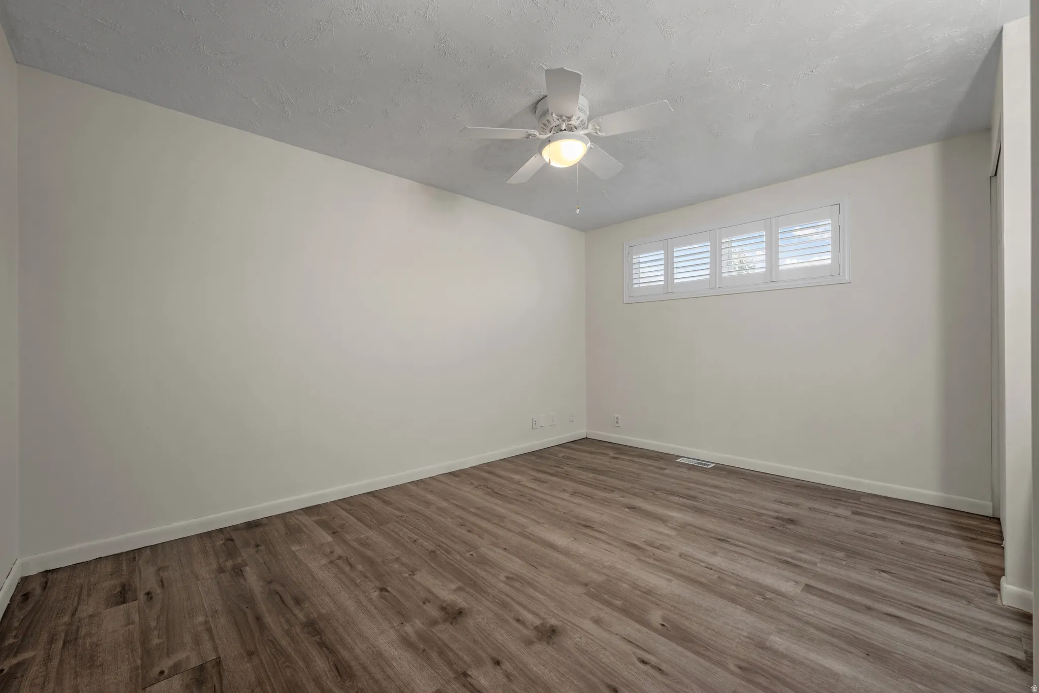 Neutral wall paint, wood-finish flooring, ceiling fan with integrated lighting, and horizontal window blinds