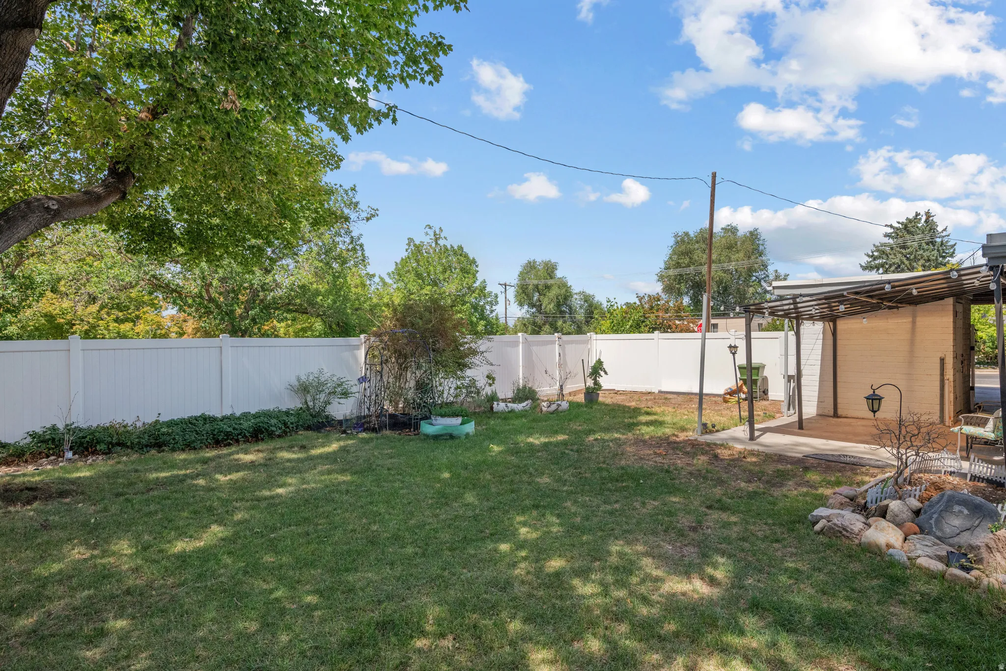 Expansive backyard featuring a privacy fence, covered patio, and mature trees