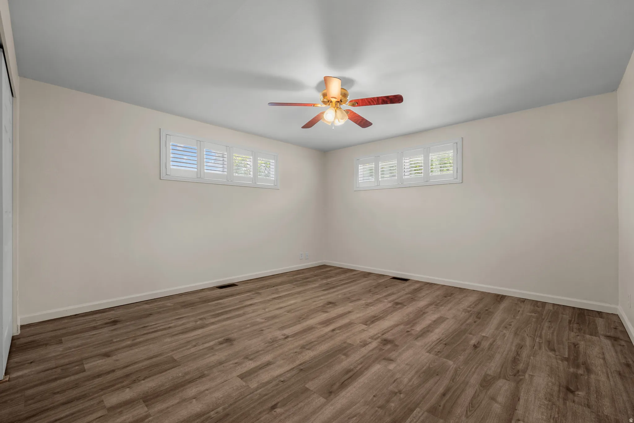 Wood-finish flooring, ceiling fan with integrated lighting, multiple windows with plantation shutters, and a sliding door