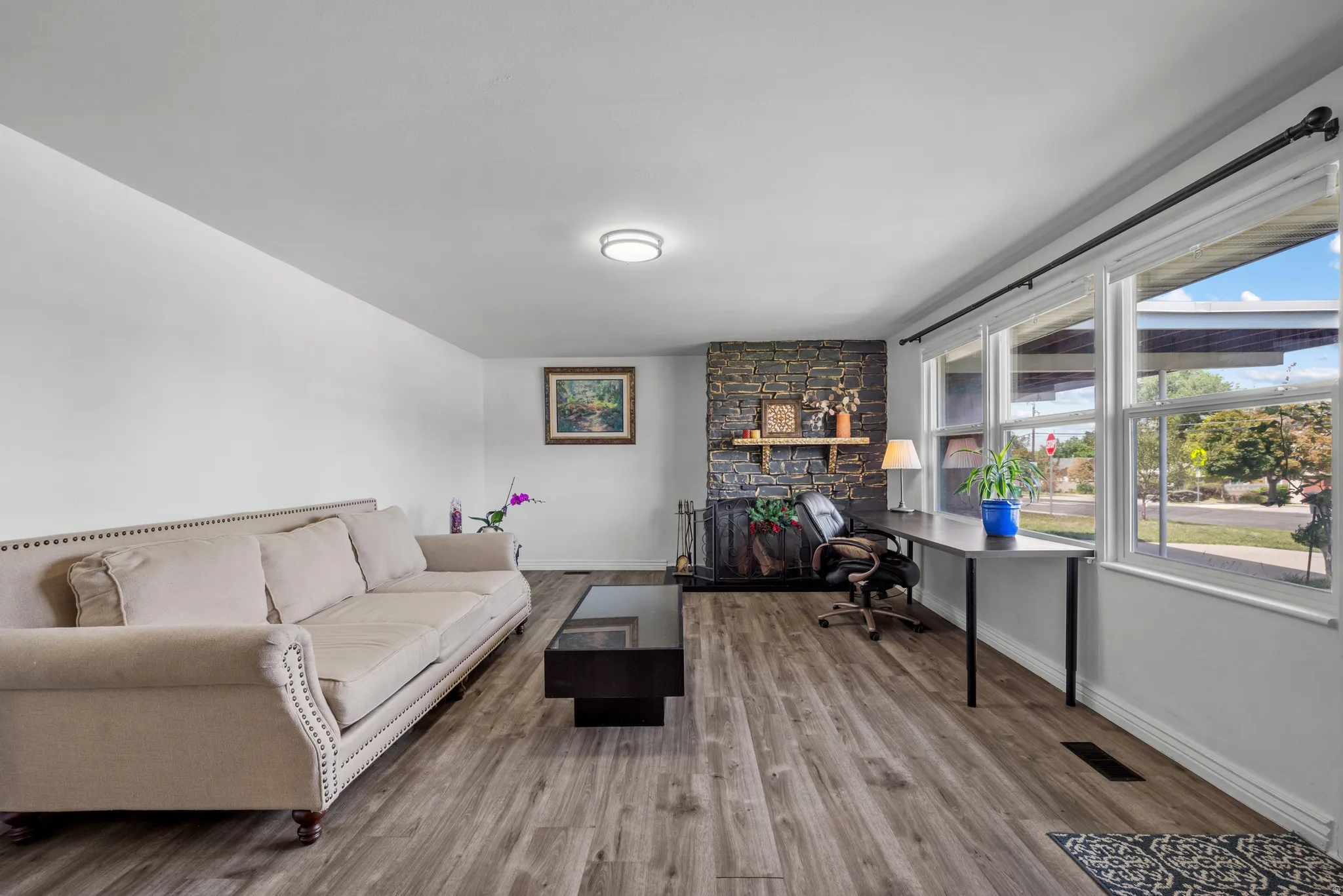 Wood-finish flooring, stone-clad fireplace with wood mantle, large multi-pane windows, and a flush-mount ceiling light